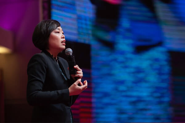 Master Suyen Lim speaking on stage with a microphone