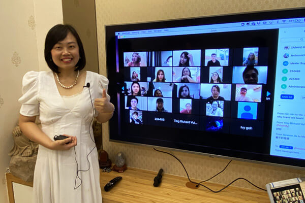Master Suyen Lim beside a screen showing her online class as a grid of students