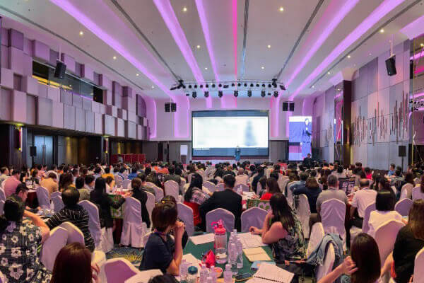 A large hall of guests seated under stage lighting at a Chinese Metaphysics event