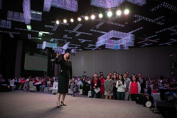 Master Suyen Lim speaking on stage to a packed auditorium
