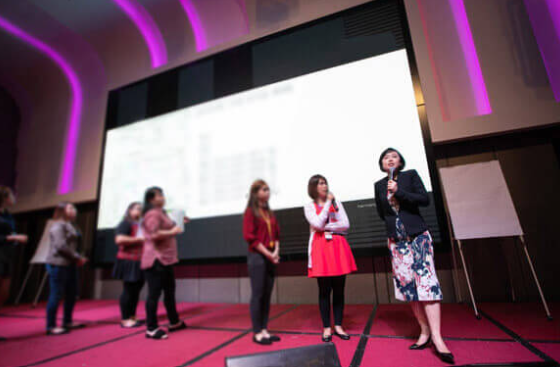 Master Suyen Lim speaking on stage beside course participants at a Chinese Metaphysics event